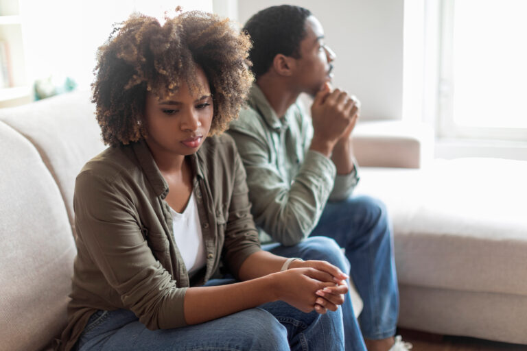 Sad african american couple sit on couch back to back